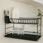Black two-tier dish rack holding white plates and glasses on a light worktop