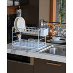 White two-tier dish rack holding plates beside a kitchen sink