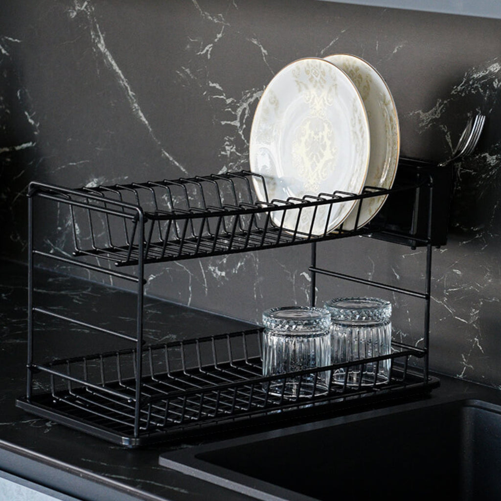 Black two-tier dish rack holding plates and glasses beside a dark kitchen sink