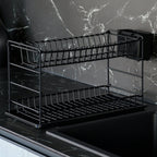 Empty black two-tier dish drainer on a worktop against a dark marble-effect wall