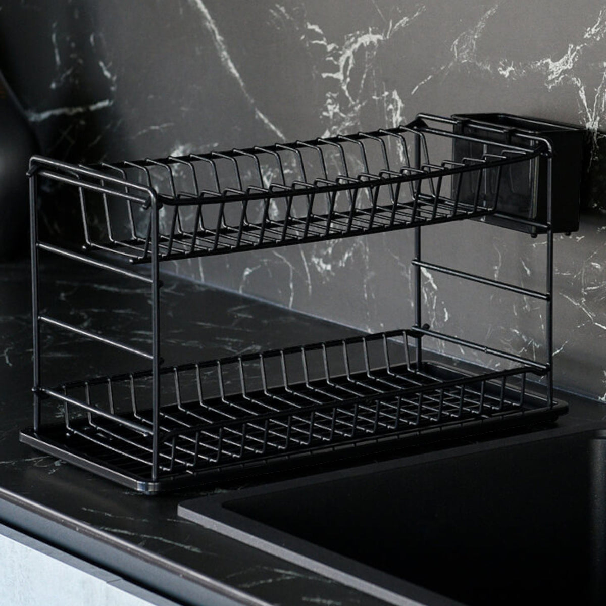 Empty black two-tier dish drainer on a worktop against a dark marble-effect wall