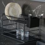 Close-up of a black two-tier dish rack holding plates, glasses and cutlery