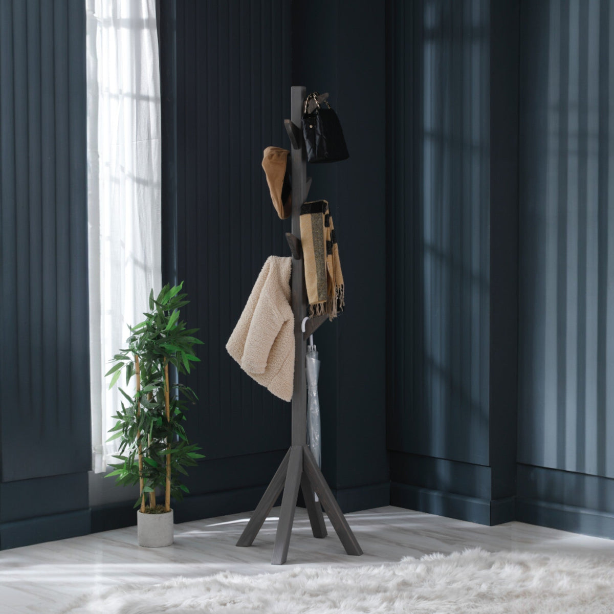 TheOwnas freestanding anthracite wooden coat rack with 9 hooks, holding jackets, bags, and scarves in a modern room.